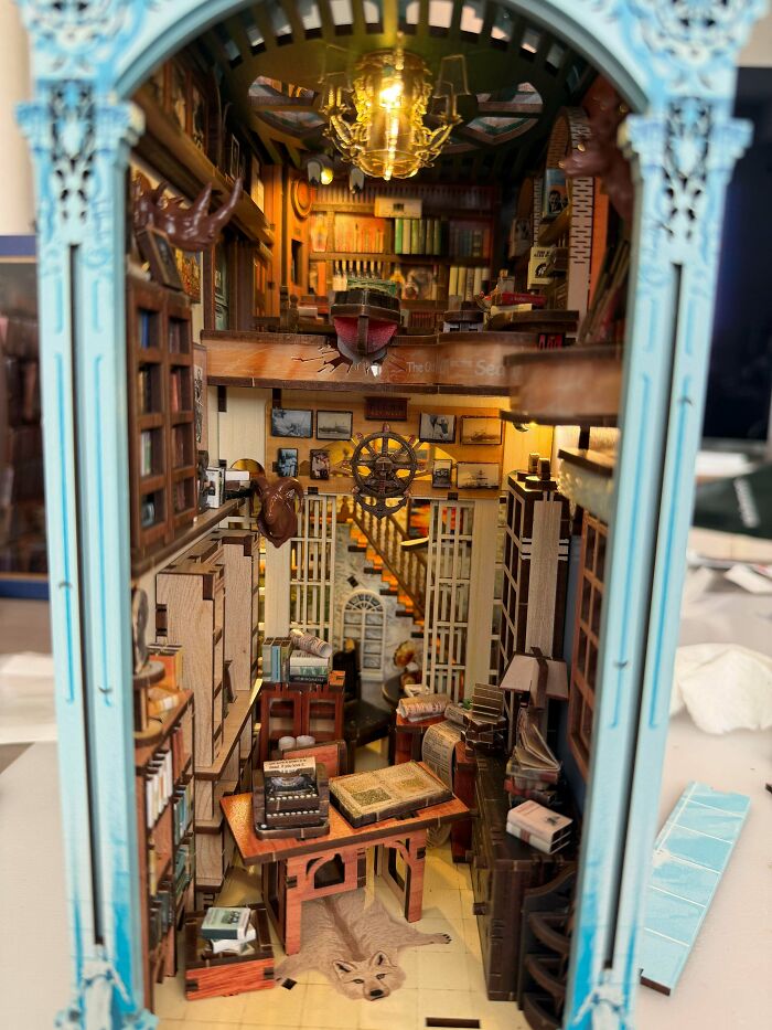 A detailed book nook showing a miniature vintage library with books and a wooden study desk