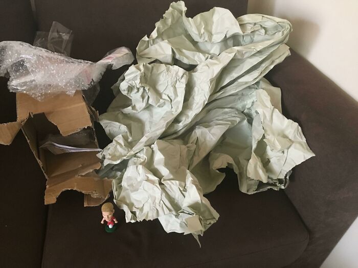 A tiny figurine next to a huge pile of paper wrap showing excessive packaging fails.