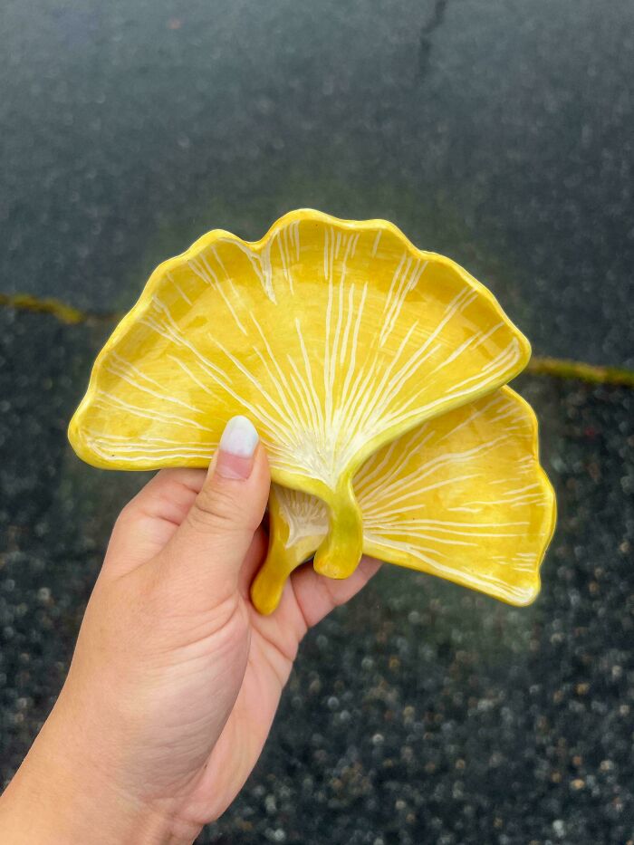 Hand holding yellow ginkgo leaf pottery creations with intricate white leaf veins.