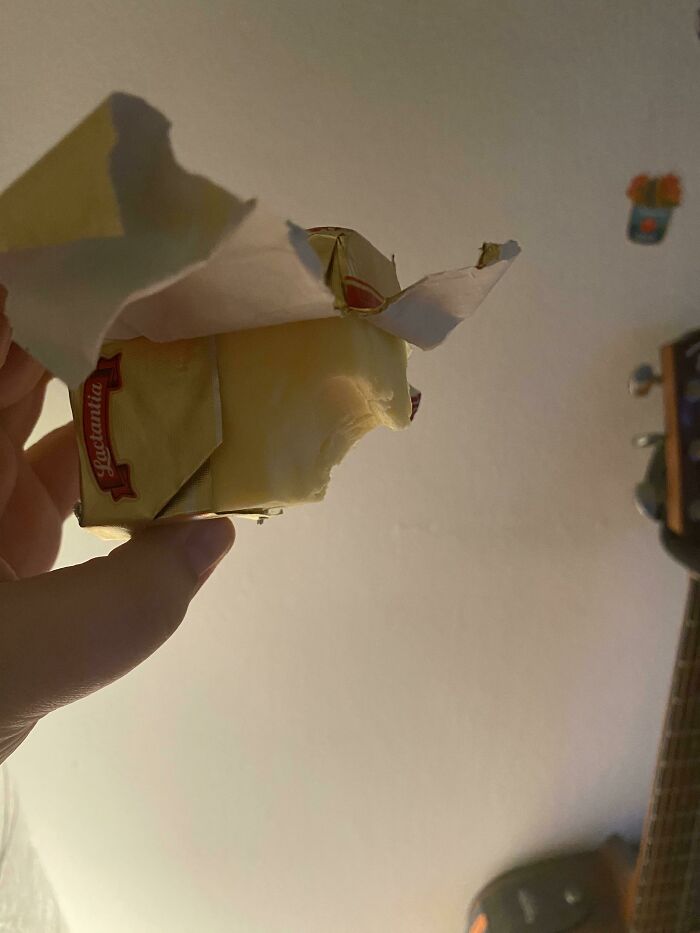 A hand holding a block of butter with a bite taken out, showing husband quirks