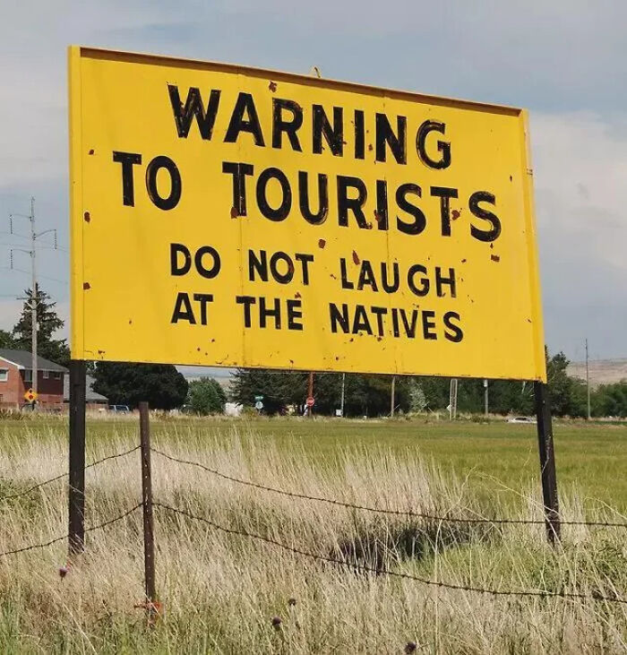 Yellow roadside sign warning tourists not to laugh at the natives, showcasing funny signs from around the world.