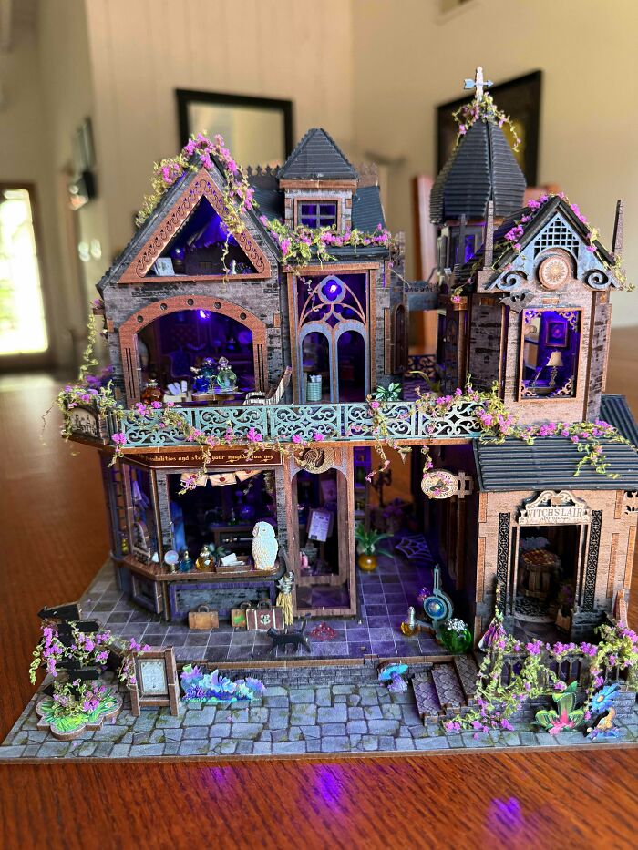 A witch-themed miniature house book nook with purple lights and floral vines