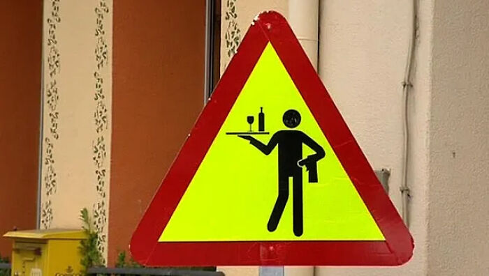 A yellow triangular road sign featuring a waiter icon, representing funny signs with mistakes