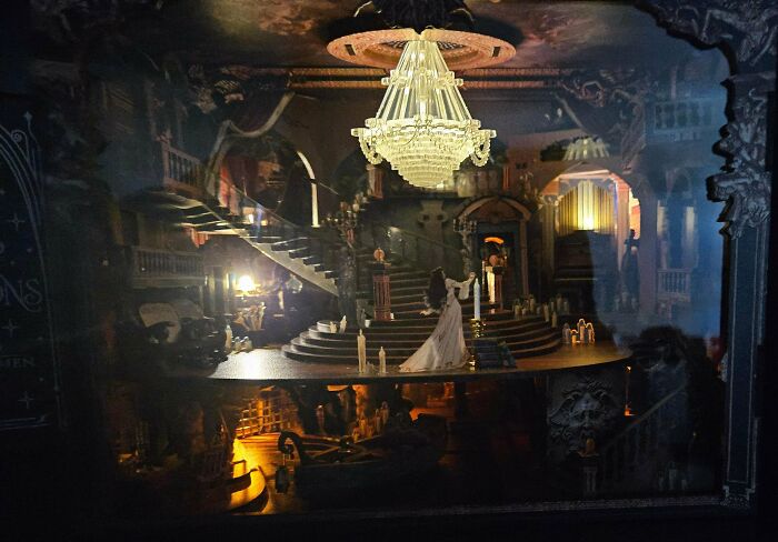 An elegant opera scene book nook with a grand chandelier, curved staircase, and a figure in white.