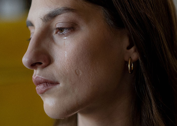 A woman crying with a tear on her cheek, showing emotional struggles of new motherhood.