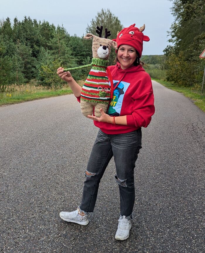Artist on road holding handmade deer crochet creature.