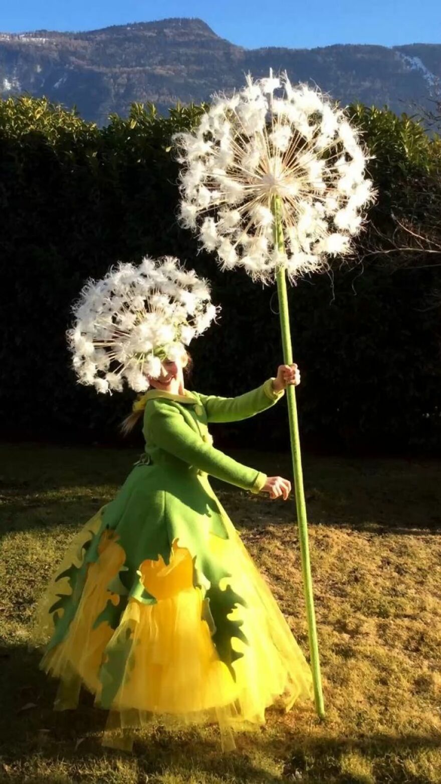 Girl dressed in a yellow and green dress holding a giant dandelion stem for a creative Halloween costume idea