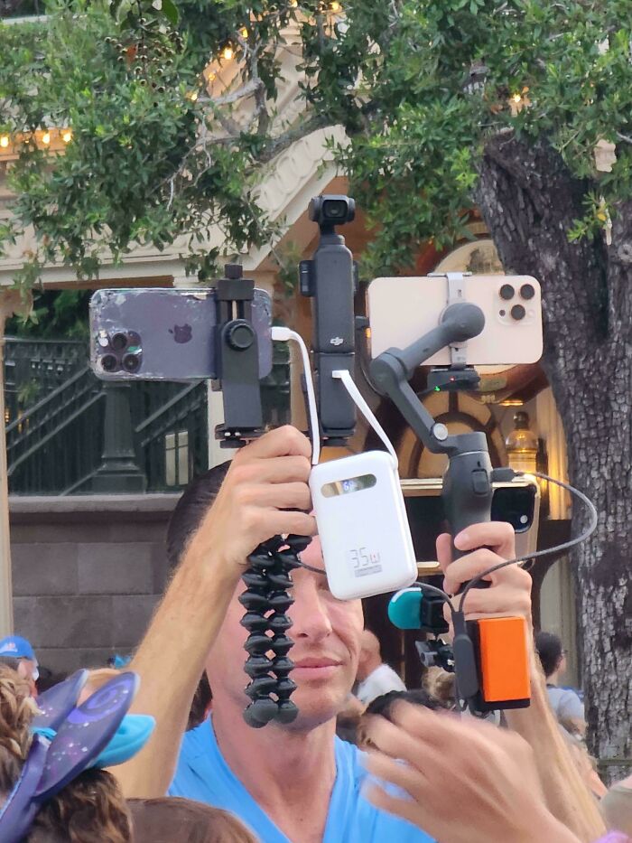 Man holding multiple recording devices at a crowded theme park like a personal content studio