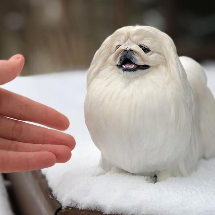 A tiny, hyperrealistic sculpture of a fluffy white Pekingese dog sitting in snow.