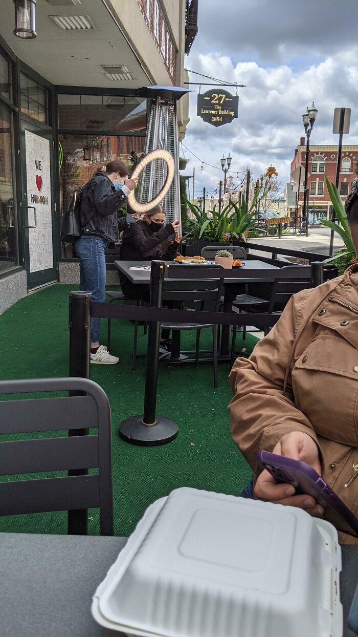 Influencers using ring lights to film food at an outdoor public restaurant patio.