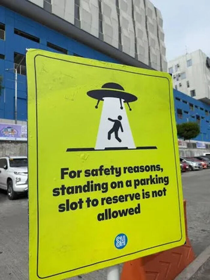 A bright yellow sign with an illustration of a UFO abducting a person, warning about parking rules.