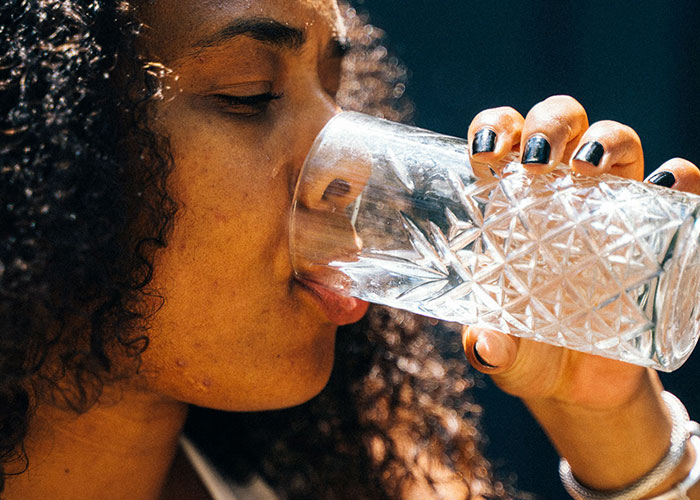 A woman drinking a glass of water, essential care during giving birth recovery and new motherhood.