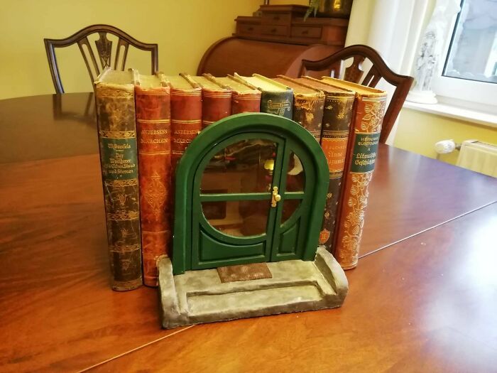 A creative book nook with a round green Hobbit-style door nested between vintage books
