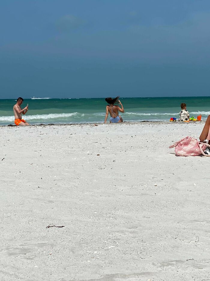 Woman posing on a public beach while a man takes photos, using public spaces as a personal content studio
