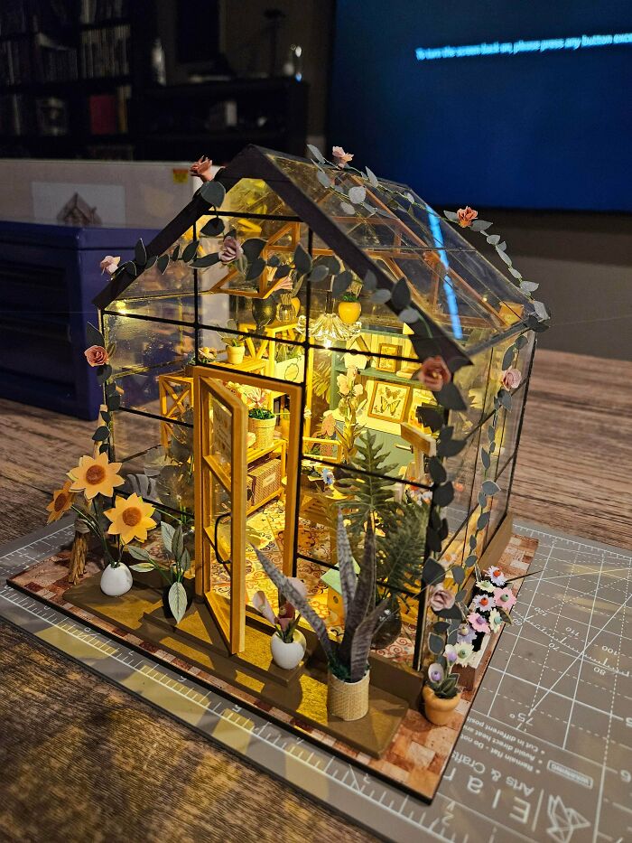 A cozy glass greenhouse miniature book nook decorated with sunflowers, tiny potted plants, and warm lighting.