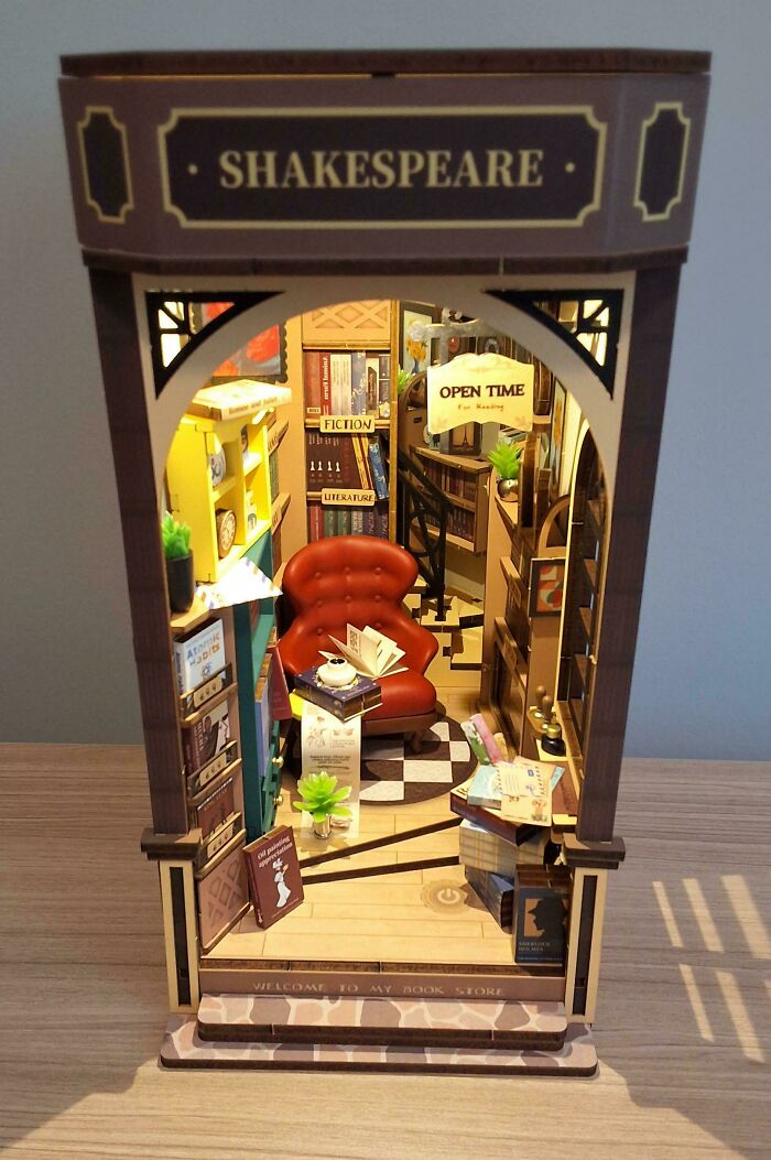A miniature Shakespeare-themed book nook showcasing a cozy bookstore interior with a red armchair.