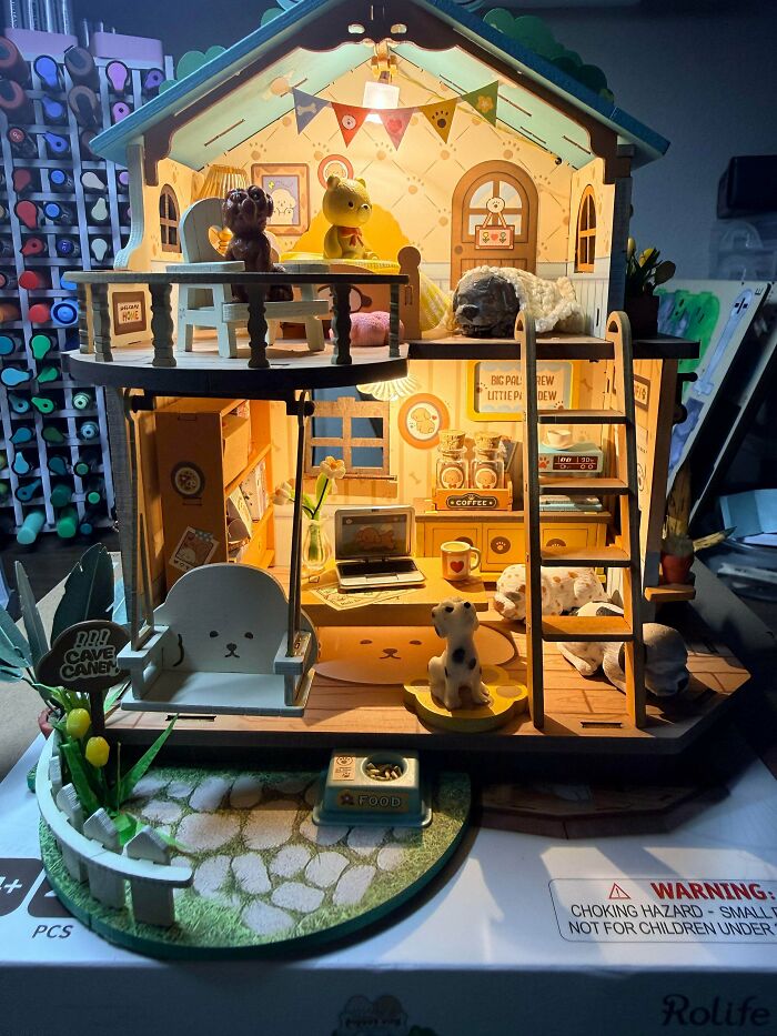 A brightly lit miniature dog house dollhouse book nook with cute puppy figurines and a small ladder.