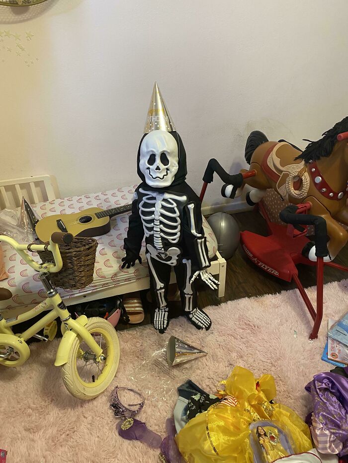 A child wearing a skeleton bodysuit and a party hat among fun Halloween costumes.