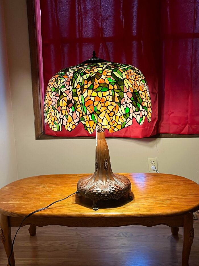 An exquisite stained glass Tiffany-style table lamp glowing on a wooden table, a thrift store find