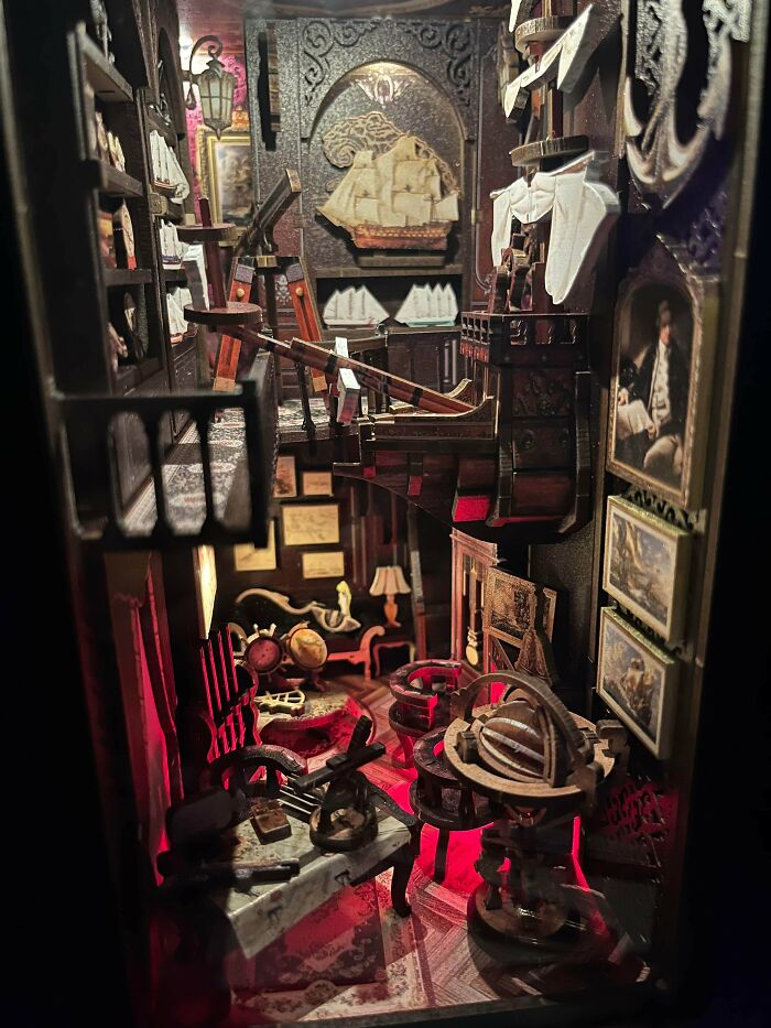 An intricate nautical-themed book nook kit displaying ships and telescopes in a tiny room.
