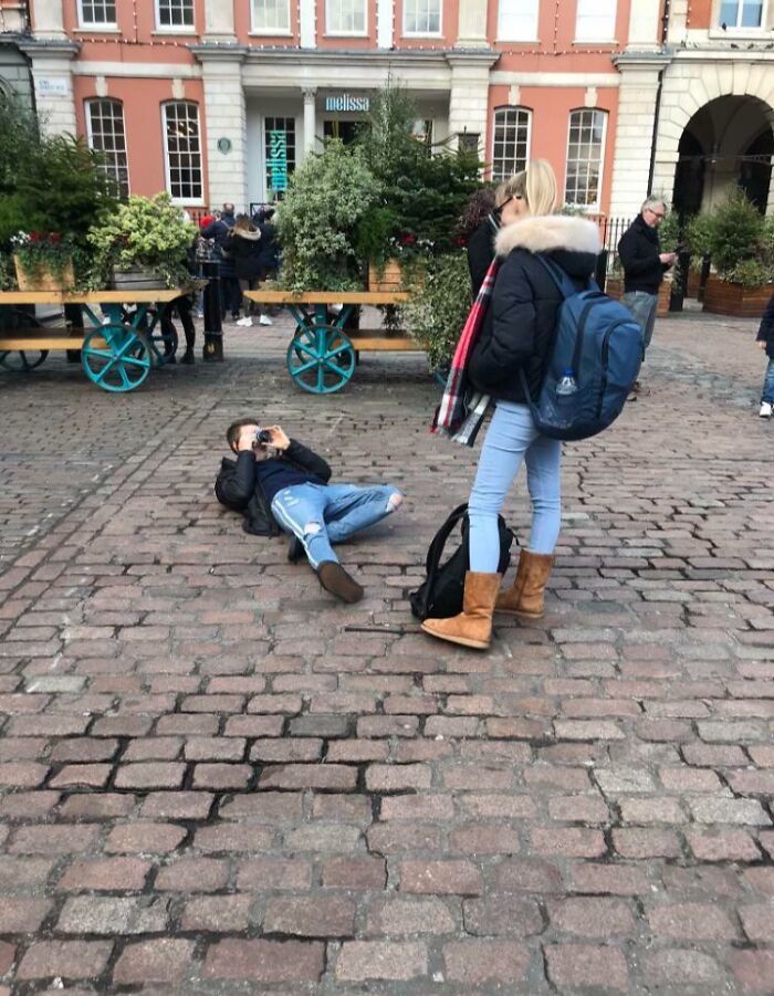 Man lying on cobblestone street taking pictures of influencers using public spaces.