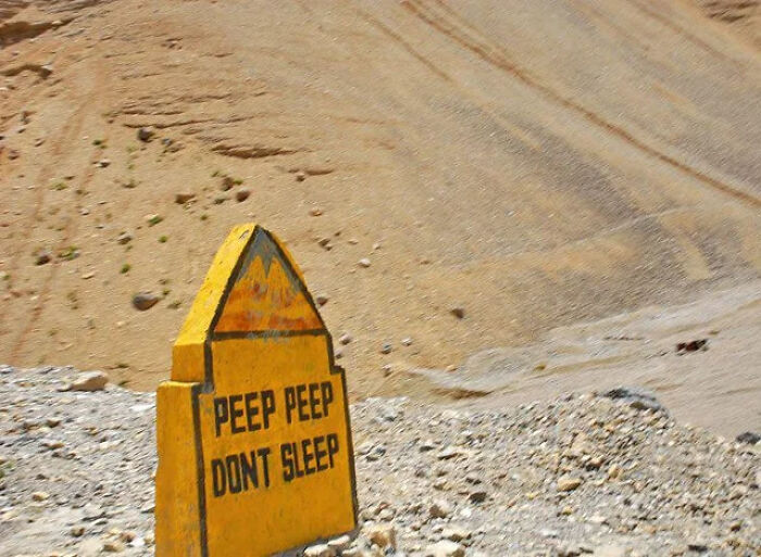 A yellow roadside milestone reading Peep Peep Don't Sleep on a mountain pass.