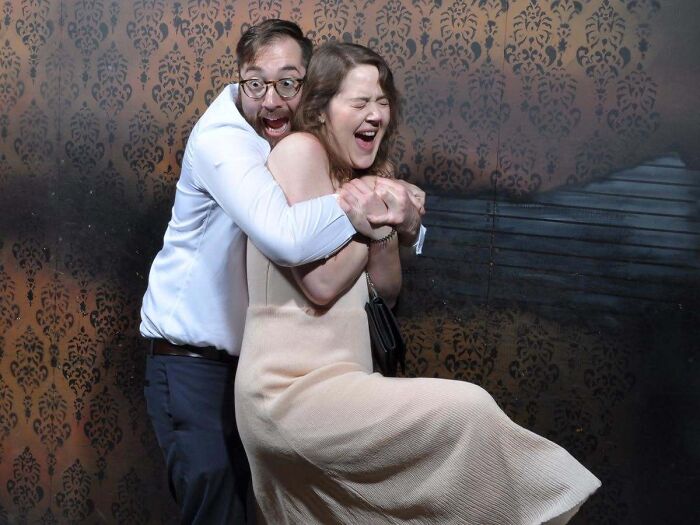 A man holds onto a woman as both scream in fear during a haunted house photo moment.