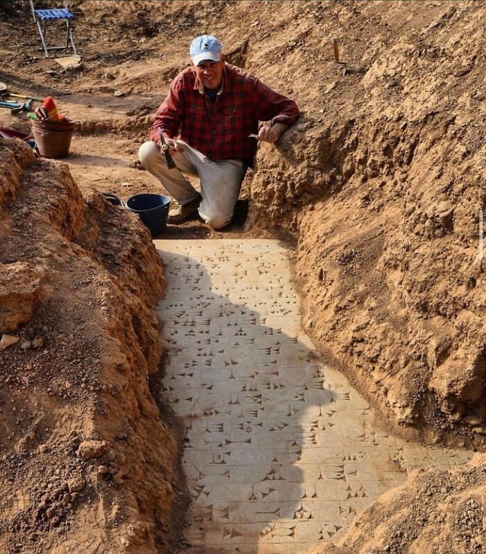 Archaeologist kneeling beside excavated cuneiform inscription carved into ancient stone.