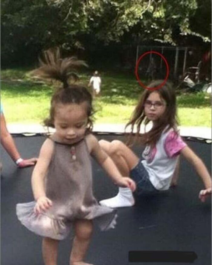 Eerie figure circled in the background behind kids playing, captured in real-life photos like a horror movie