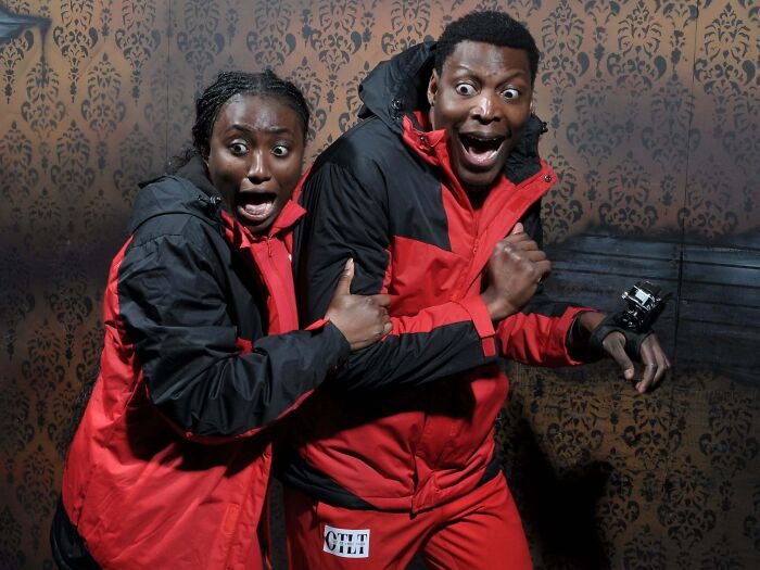 Scared couple in matching red jackets reacting dramatically in a funny haunted house photo