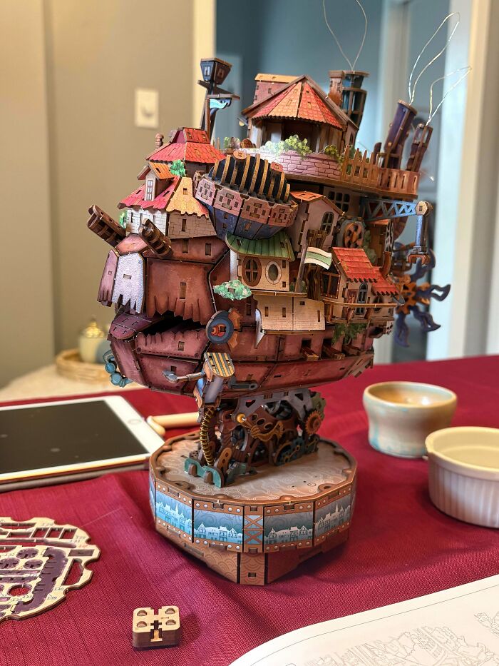 An intricate 3D puzzle model of Howl's Moving Castle assembled on a red table.