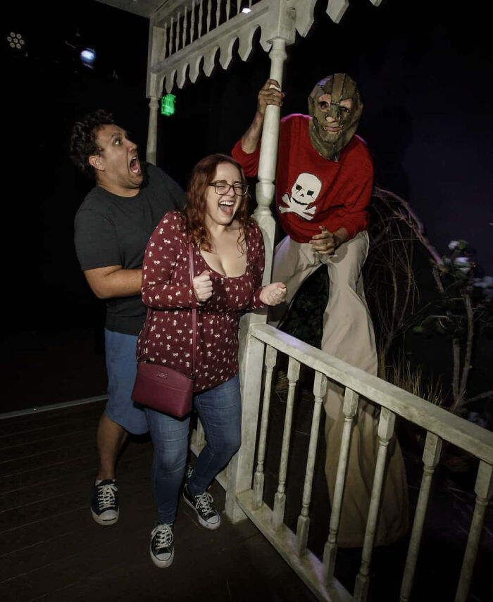 Scared couple screaming as a masked performer jumps out in a haunted house