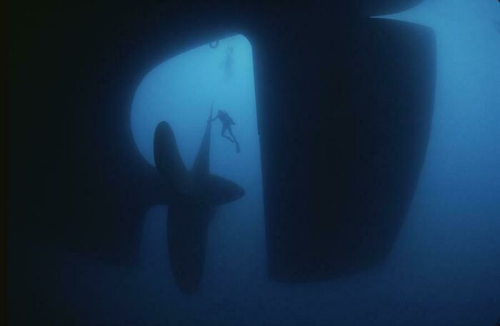 Scuba diver next to a massive ship propeller, showcasing mysteries at the bottom of the ocean.