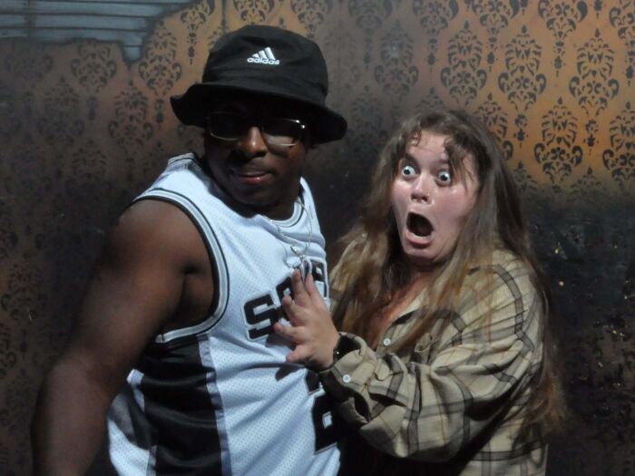 Scared woman grabbing a calm man in a hilarious haunted house photo moment
