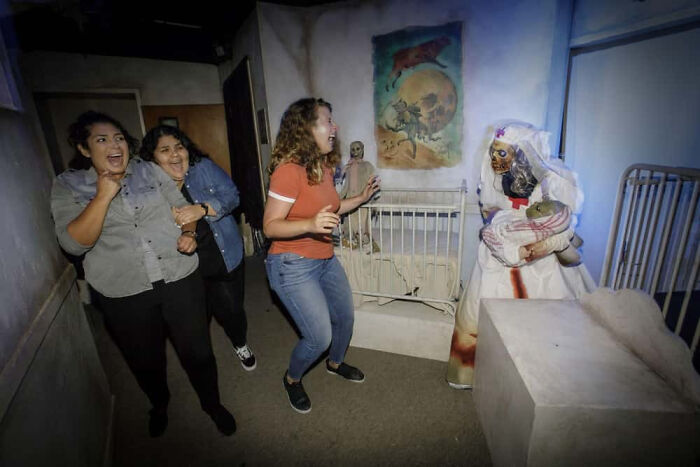 Terrified visitors scream inside a dark nursery setting at a haunted house attraction.