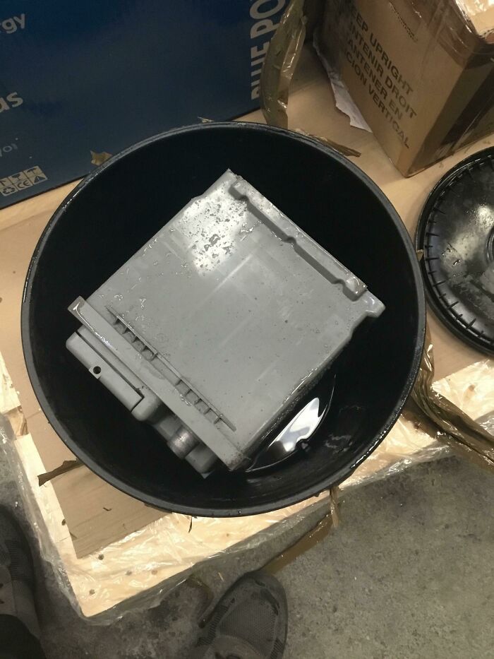 Grey car battery submerged in a black bucket of liquid showing packaging fails