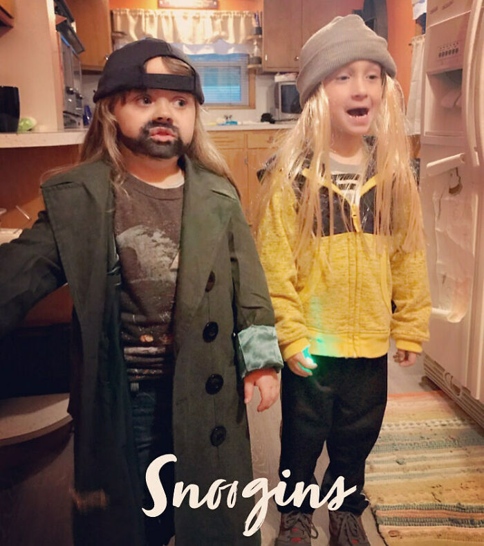 Two young kids dressed in Jay and Silent Bob Halloween costumes posing indoors with funny fake facial hair.