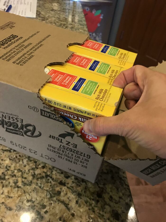 A hand trying to open a box of cocoa mix showing a packaging fail with mismatched perforated opening strips.