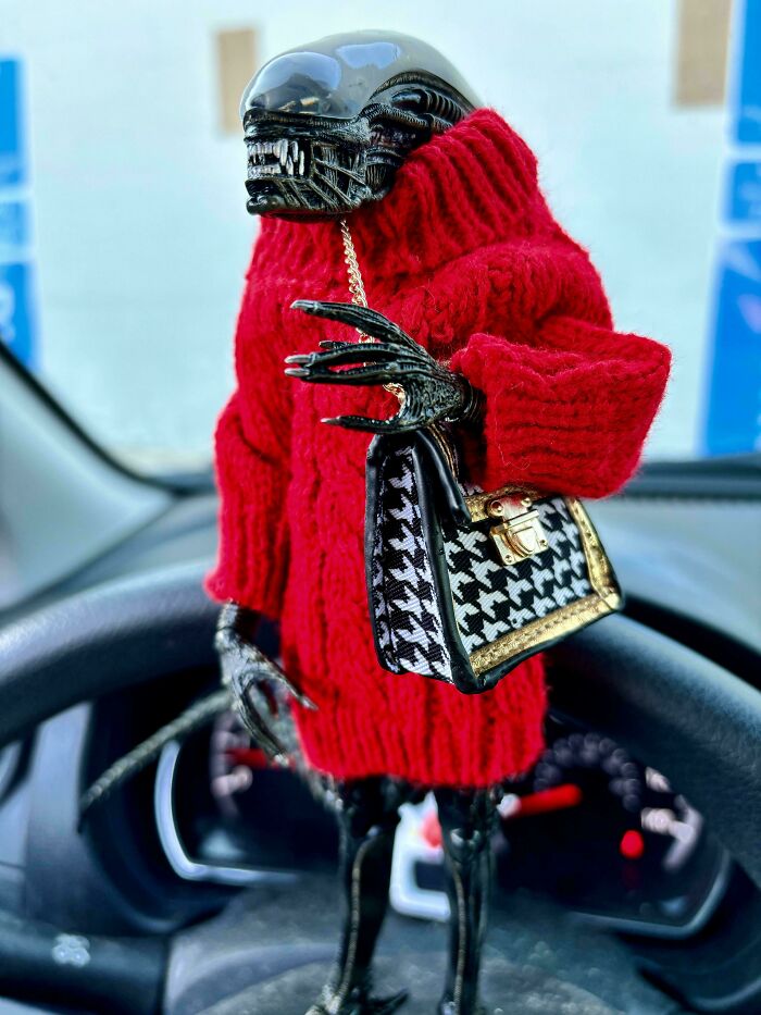 An Alien action figure wearing a red knitted sweater and holding a tiny purse