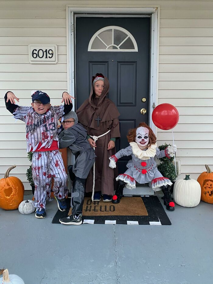 Four kids wearing spooky zombie, monk, and Pennywise kids Halloween costumes on a porch.