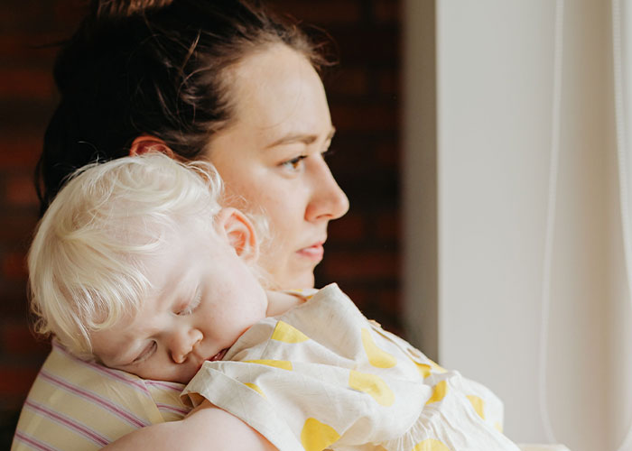 A tired mother embracing her sleeping toddler during early new motherhood