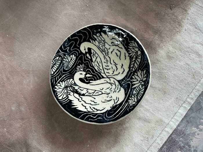 A black and white ceramic plate featuring swans and water lilies as part of pottery creations