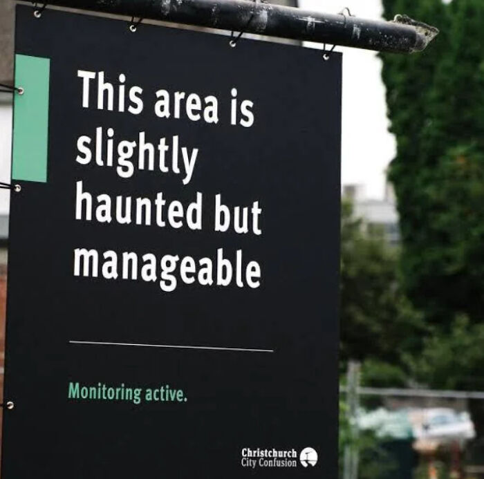 A black sign with humorous text saying this area is slightly haunted but manageable, displaying funny signs.