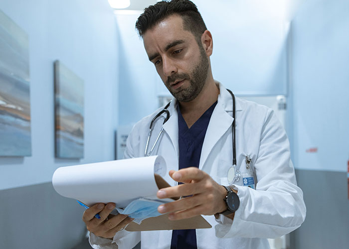 A male doctor reviewing medical charts in a hospital hallway during post-giving birth care.