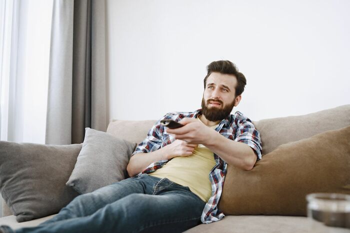 A frustrated man watching TV on the couch, reflecting on relationship revenge stories.