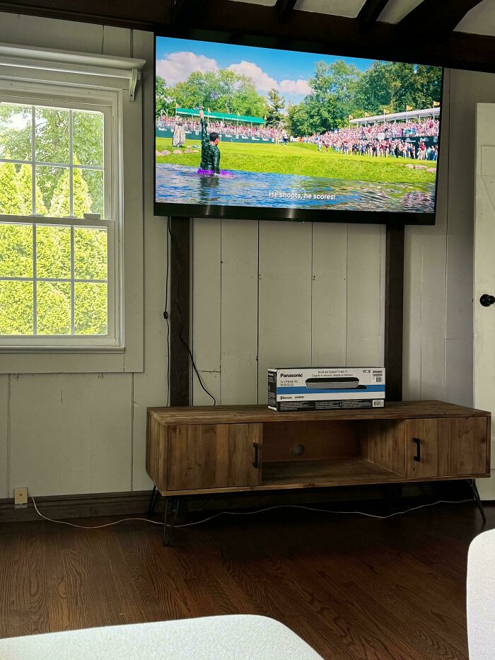 A television mounted high on a wall with a wooden console table underneath