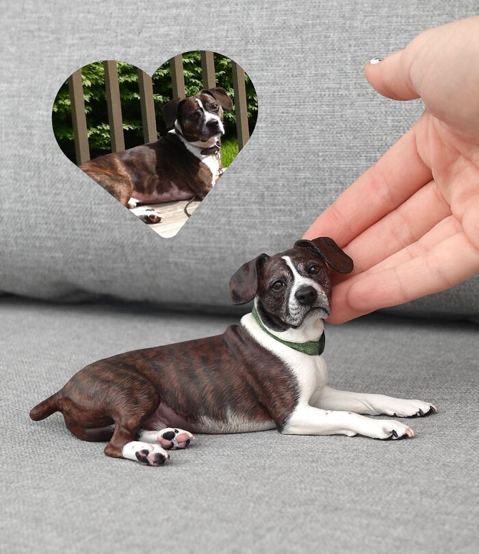 Handmade hyperrealistic sculpture of a lying brindle dog beside a reference photo.