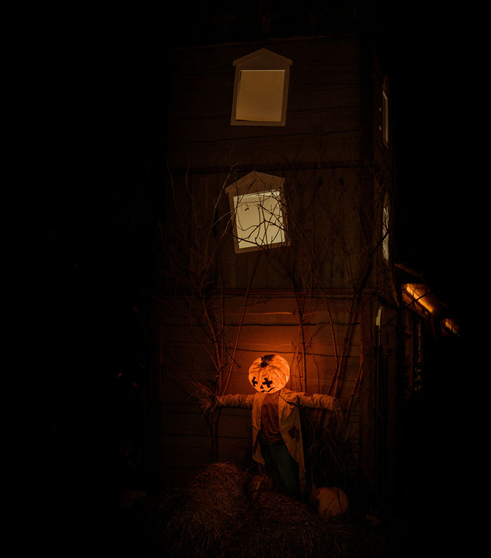 A eerie glowing pumpkin scarecrow standing outside a dark house for scary Halloween stories.