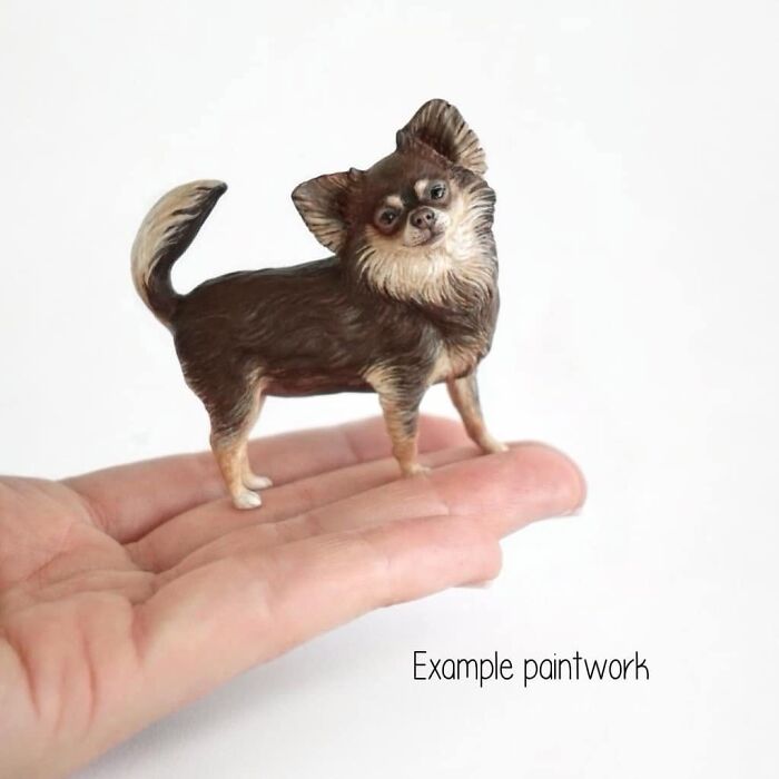 A hand supporting a tiny, hyperrealistic sculpture of a Chihuahua pet.