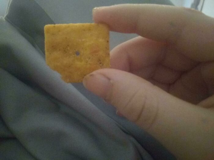A square-shaped tortilla chip held up to show manufacturing and bad packaging fails.
